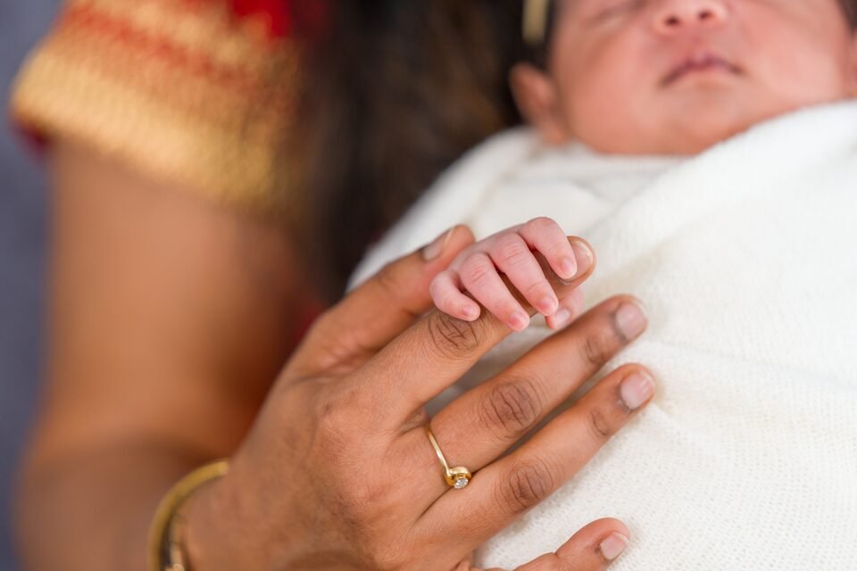 Close view of a mother’s bangled hands cradling her newborn’s head and tiny fingers