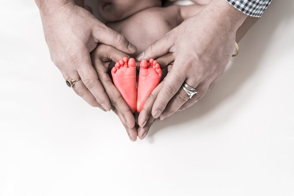 Two parents’ hands forming a heart around their newborn’s feet