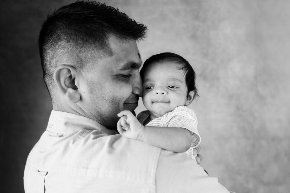 Black and white photograph of a father holding his baby cheek to cheek, both eyes closed