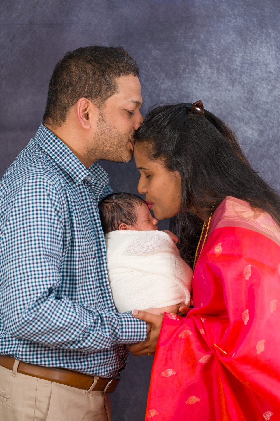 Father leaning down to kiss his newborn while the mother looks on