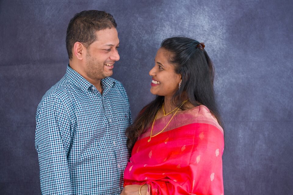 New parents turned towards one another, mid-conversation, against a painted studio backdrop
