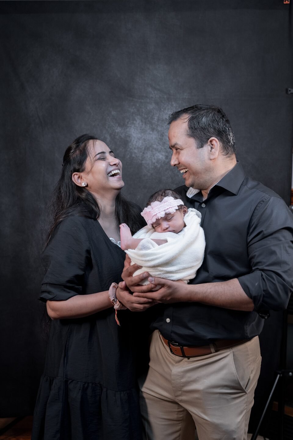 Parents laughing together while holding their newborn daughter