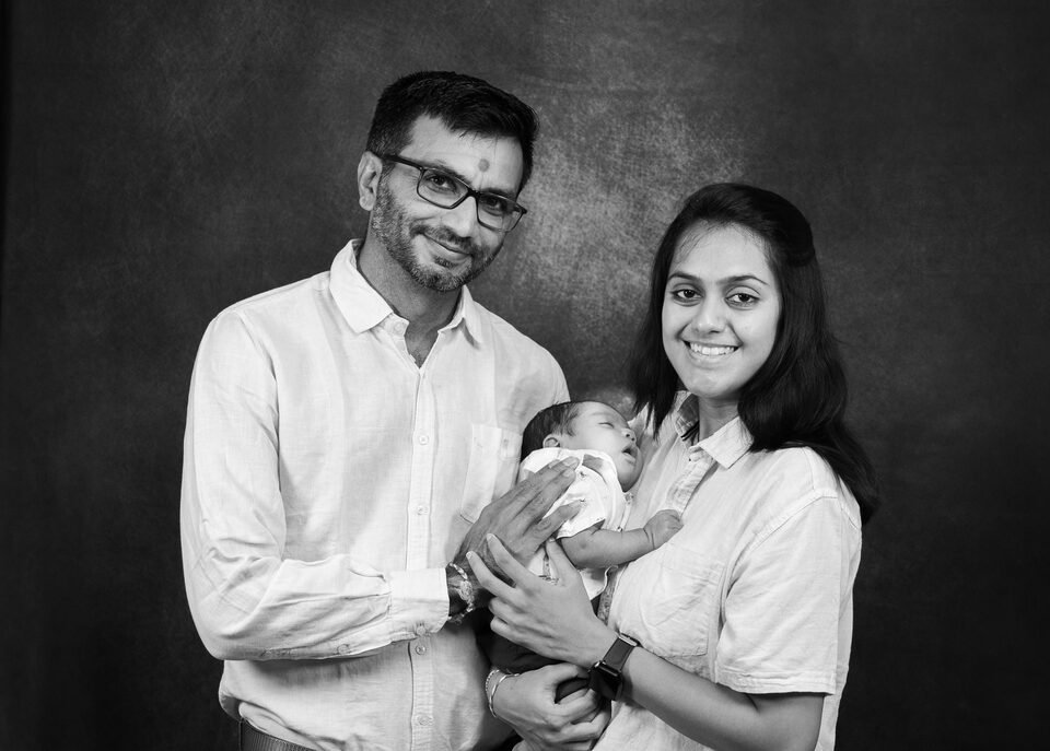 Black and white portrait of new parents holding their baby against a textured painted backdrop