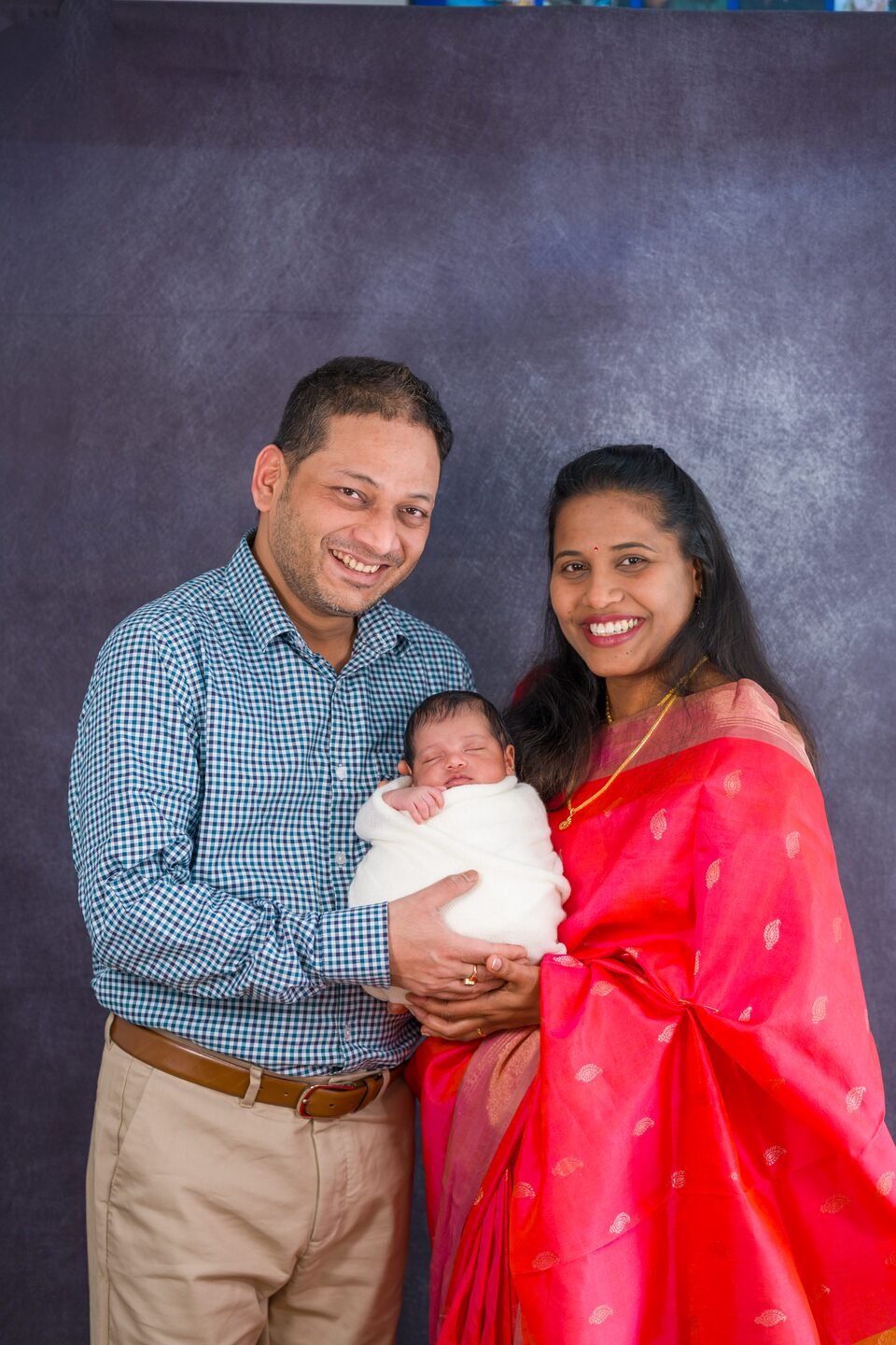 Mother and father standing close together, holding their newborn between them