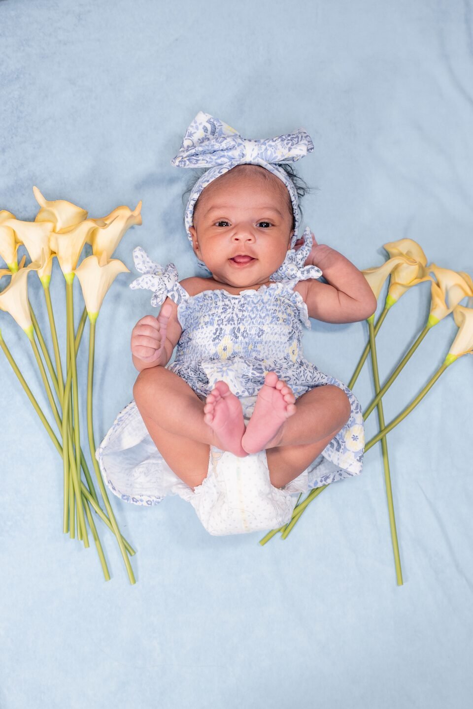 Baby lying on a pale blue blanket framed by fresh calla lilies