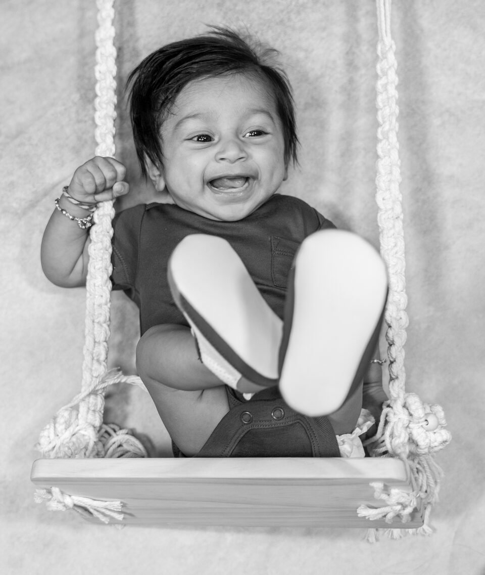 Black and white photograph of a laughing baby seated on a wooden studio swing
