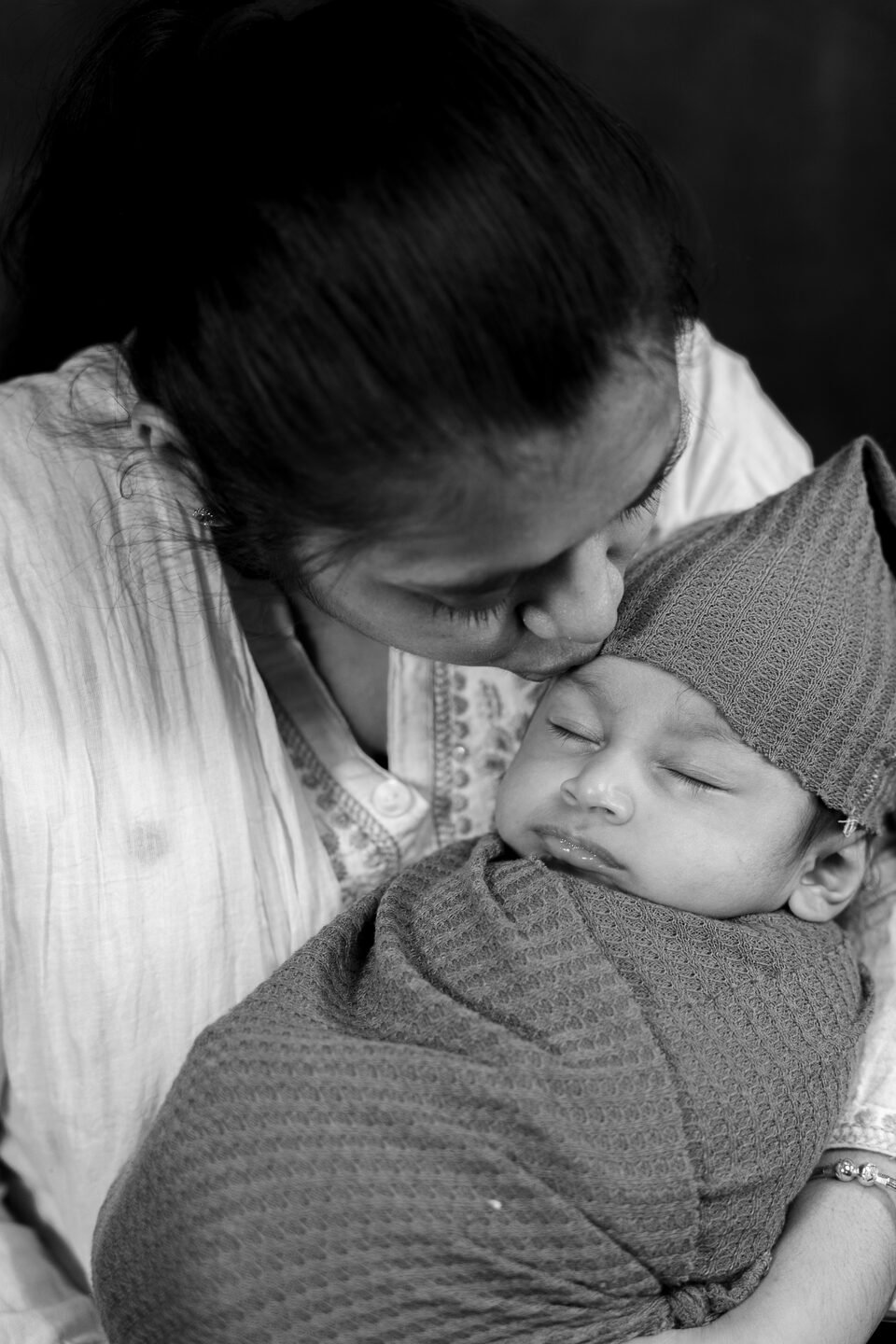 Black and white photograph of a mother kissing the top of her newborn’s head