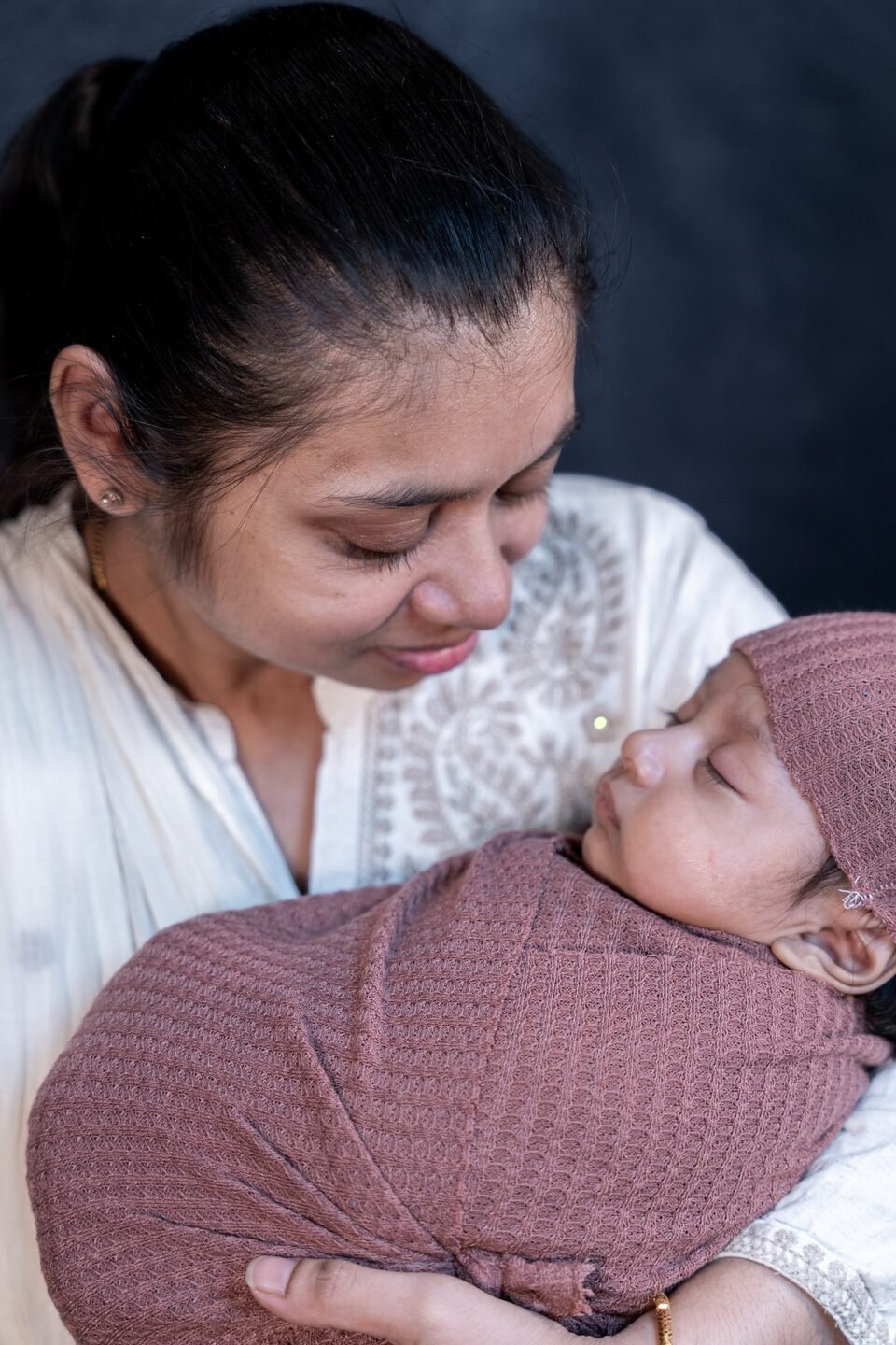 Mother in white looking down at her newborn, wrapped in dusty rose