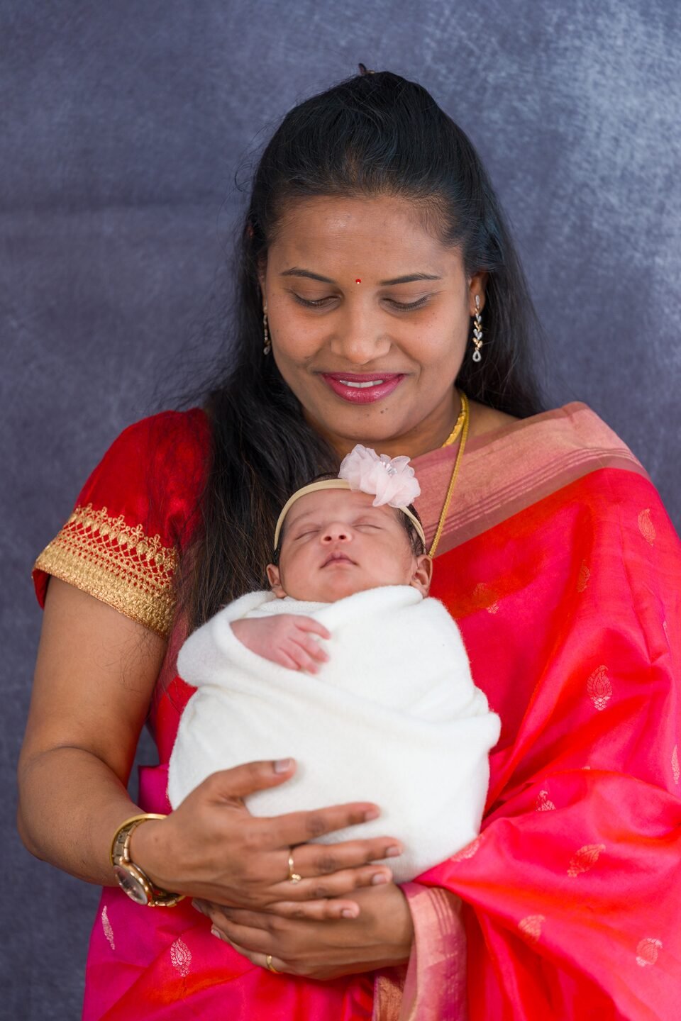 Mother in a red saree holding her newborn daughter against her shoulder