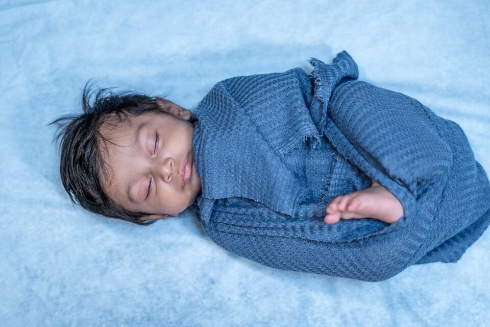 Newborn asleep in a blue knitted outfit on a soft blue blanket