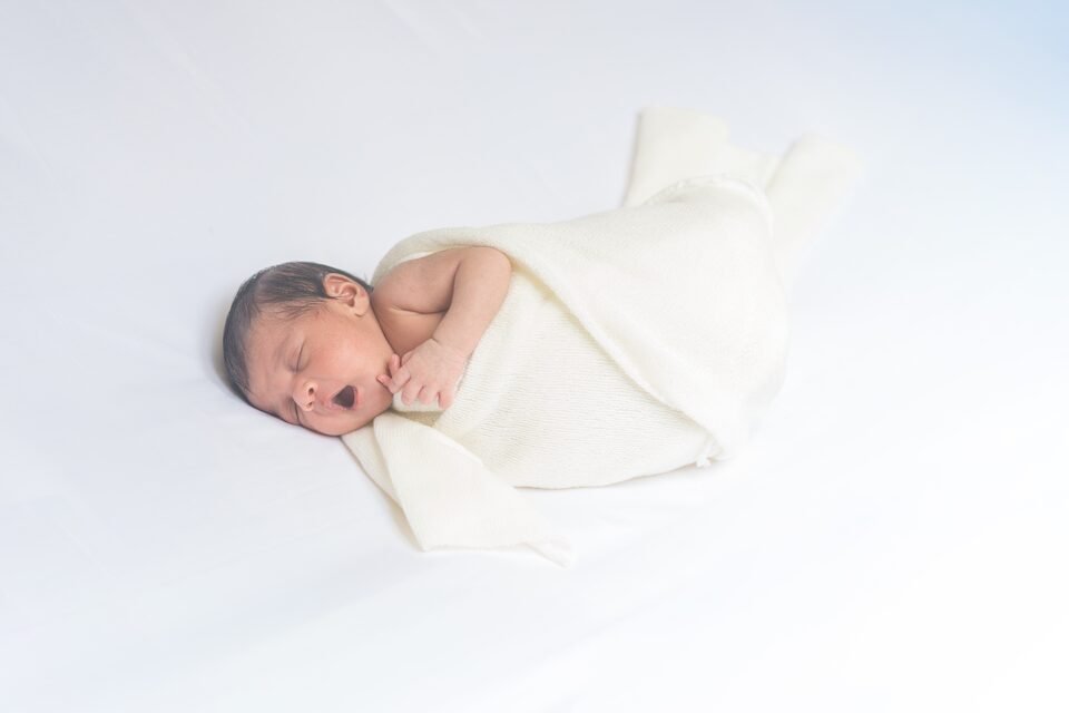 Newborn curled asleep in an ivory swaddle on white linen