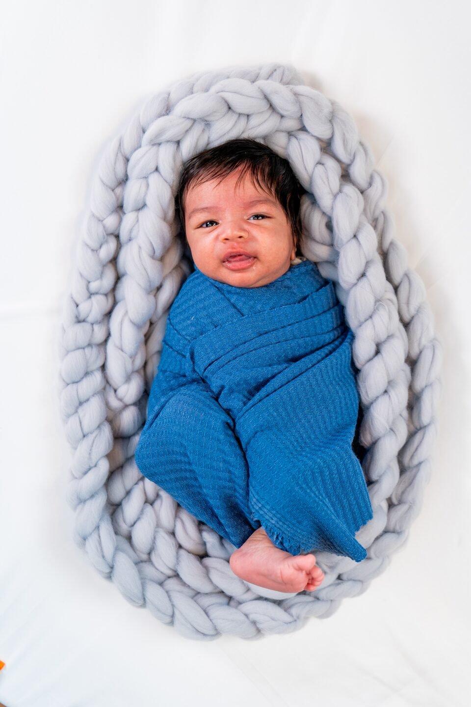 Newborn awake in a deep indigo wrap, settled in a braided wool nest