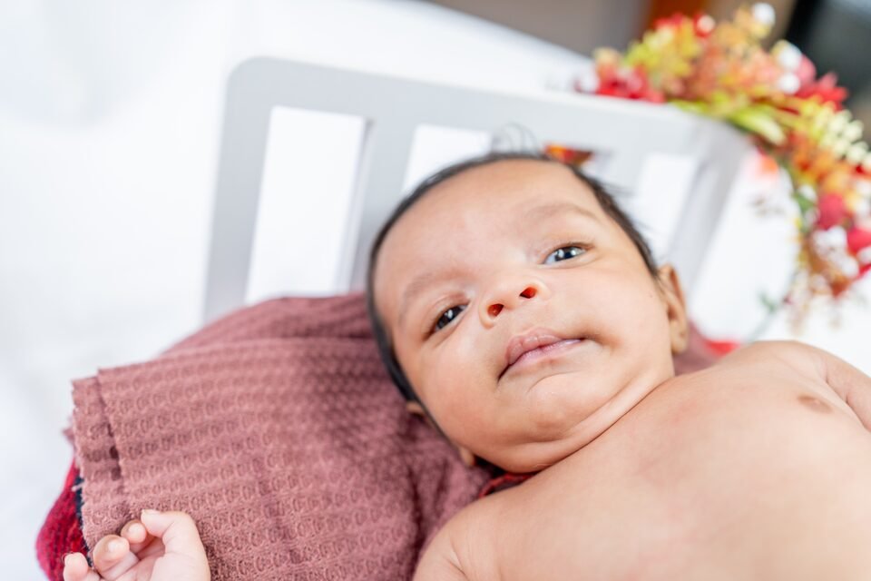 Newborn lying awake under a dusty rose blanket in a small white bed