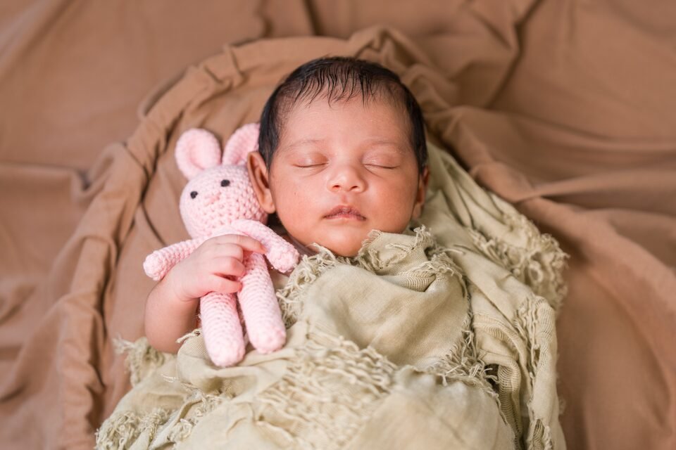 Sleeping newborn in a sage wrap beside a small crocheted bunny