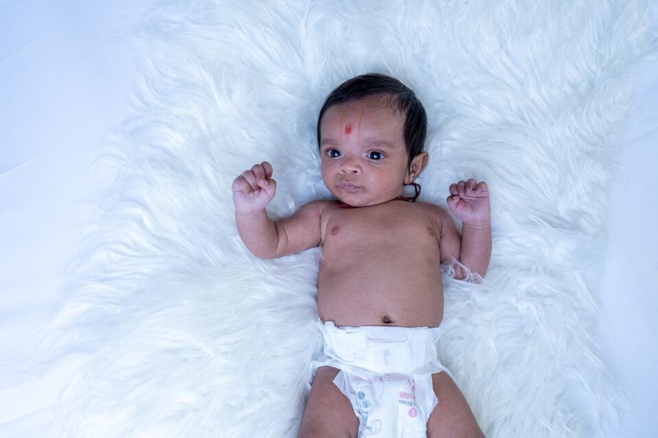 Newborn stretching both arms open while lying on a white fur blanket