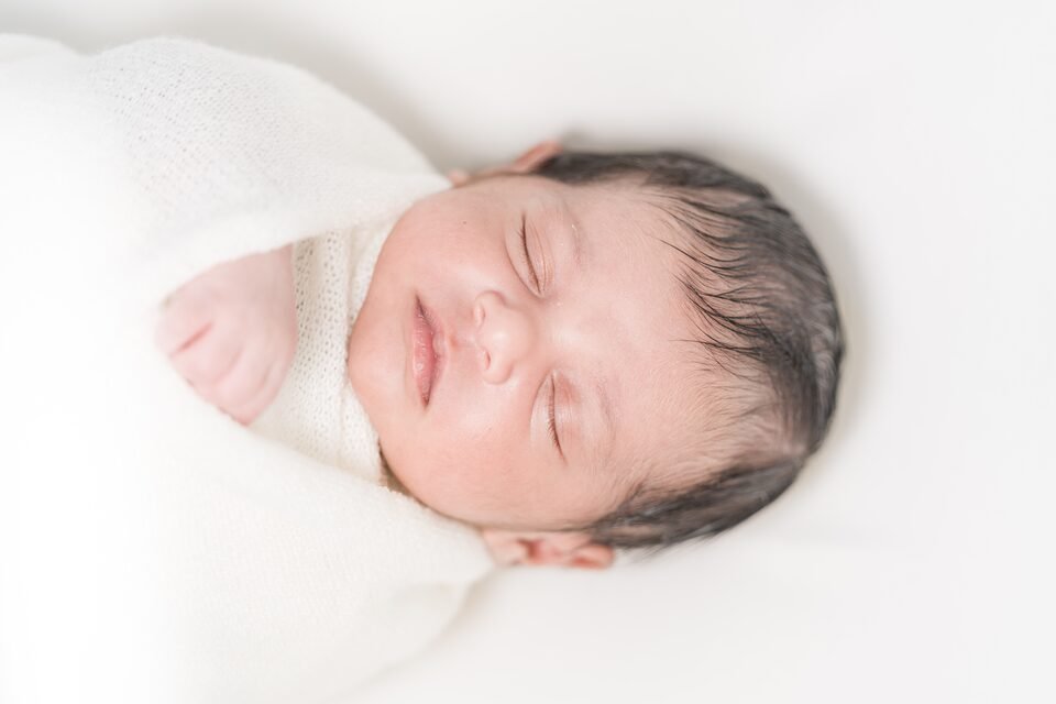 Newborn asleep in a white wrap against a bright, softly lit backdrop